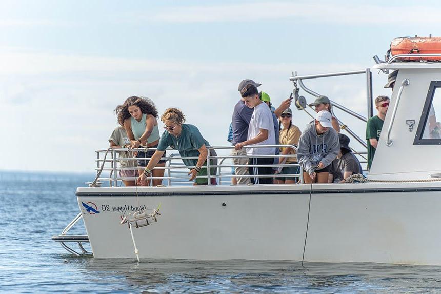 Students lowering a water collection device into the Mount Hope Bay. 